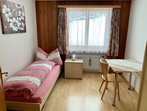 A small bedroom with a single bed, a bedside table, a chair, and a window with curtains. - Bergröschen Appartement/Fewo 5-Bettwohnung by Interhome (Saas-Grund)