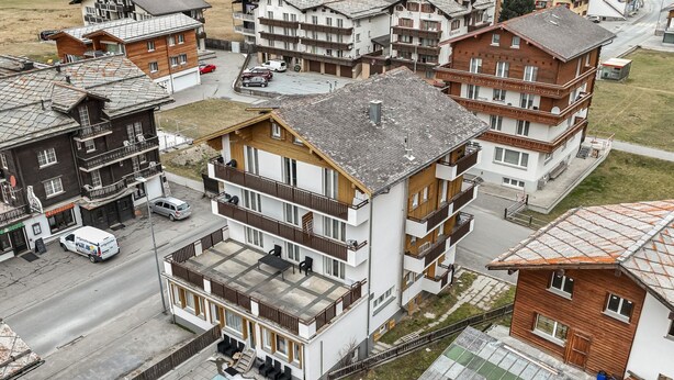 A multi-story building with balconies, a ground-level patio, and a street view. - Haus Astoria Studio Apt # 6 by Interhome (Saas-Grund)