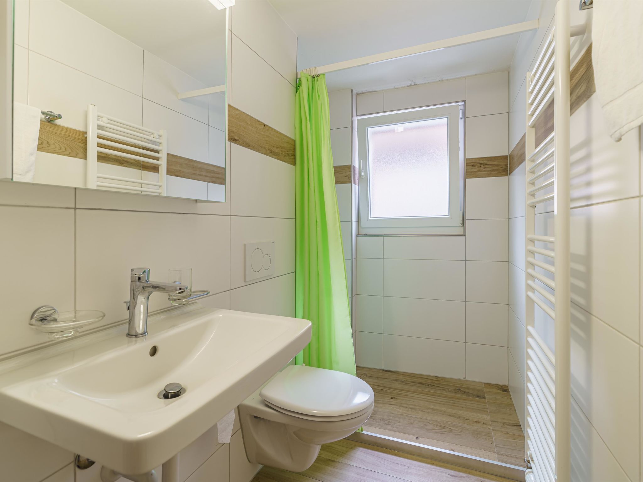 Un baño con un lavabo blanco, un inodoro, una ducha con cortina verde y un ventanal.