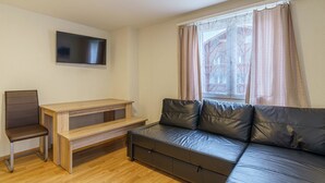 A small, furnished room with a sofa, a chair, a wooden table, and a flat-screen TV mounted on the wall. - Haus Astoria Studio Apt # 6 by Interhome (Saas-Grund)