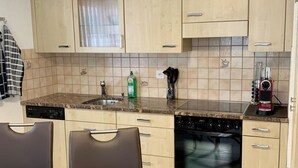 Een moderne keuken met lichte houten kastjes, een granieten aanrecht, een vaatwasser en een eethoek met een glazen tafel en stoelen.