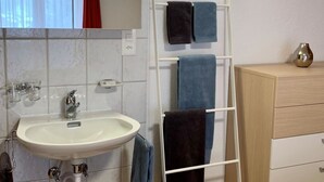 Een badkamer met een wastafel, spiegel, handdoekrek en een klein prullenbakje.