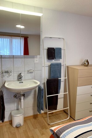 Une salle de bain équipée d’un lavabo, d’un miroir, d’un porte-serviettes et d’une petite poubelle.