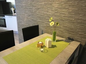 A dining area with a table set for two, a vase with yellow flowers, and a kitchen in the background. - Alcazar Apartments Appartement/Fewo Wohnung 3b by Interhome (Saas-Grund)