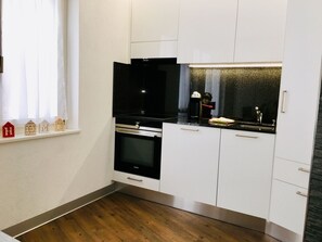 Una cocina compacta con muebles blancos, una estufa negra y un ventanal con cortinas.