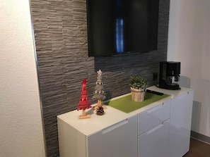 Una cocina moderna con salpicadero de piedra, un televisor de pantalla plana montado sobre un gabinete blanco y una cafetera en la encimera.