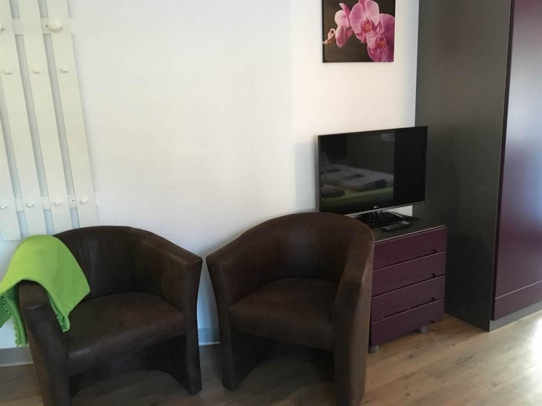 Et værelse med to brune lænestole, et fjernsyn på et stativ, et maleri af en pink orkidé og en hvid radiator.