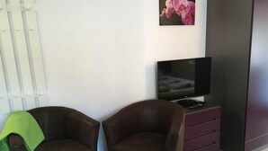 Ein Zimmer mit zwei braunen Sesseln, einem Fernseher auf einem Schrank, einem Gemälde einer rosa Orchidee und einem weißen Heizkörper.
