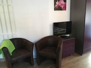 Una habitación con dos sillones marrones, un televisor sobre un mueble bajo, un cuadro de una orquídea rosa y un radiador blanco.