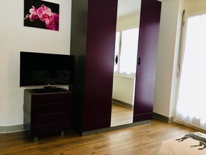 A room with a television on a stand, a wardrobe, and a door leading to another room. - Alcazar Apartments Studio Wohnung 3 by Interhome (Saas-Grund)