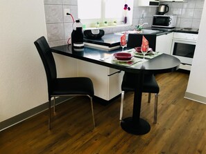 A modern kitchen with a black countertop, white cabinets, and a dining area with two black chairs. - Alcazar Apartments Studio Wohnung 3 by Interhome (Saas-Grund)