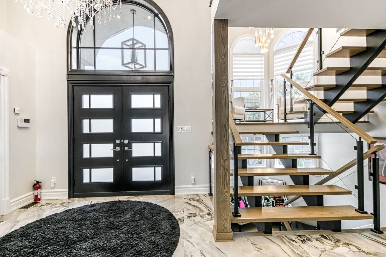 Un intérieur moderne avec une porte noire, un escalier à marches en bois et un lustre.