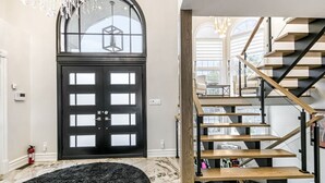 A modern interior with a black door, a staircase with wooden steps, and a chandelier. - Luxe Lake Front | Sauna | Pool Table | FirePit (Greater Sudbury)