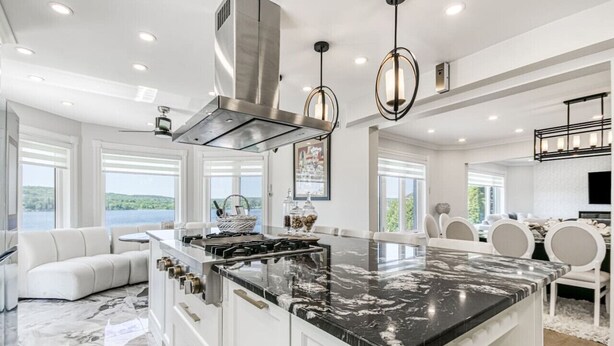 A modern kitchen with a large island, white cabinetry, and a view of the outdoors. - Luxe Lake Front | Sauna | Pool Table | FirePit (Greater Sudbury)