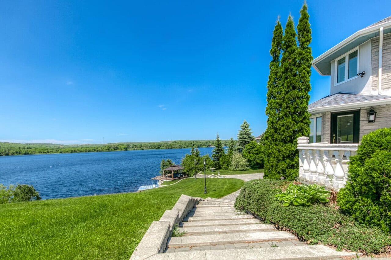 Une maison avec un escalier en pierre menant à une terrasse d’où l’on a vue sur un lac.