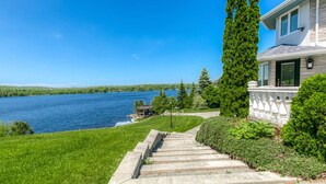 A house with a stone staircase leading to a deck overlooking a lake. - Luxe Lake Front | Sauna | Pool Table | FirePit (Greater Sudbury)