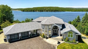 A large house with a garage, a driveway, and a lake view. - Luxe Lake Front | Sauna | Pool Table | FirePit (Greater Sudbury)