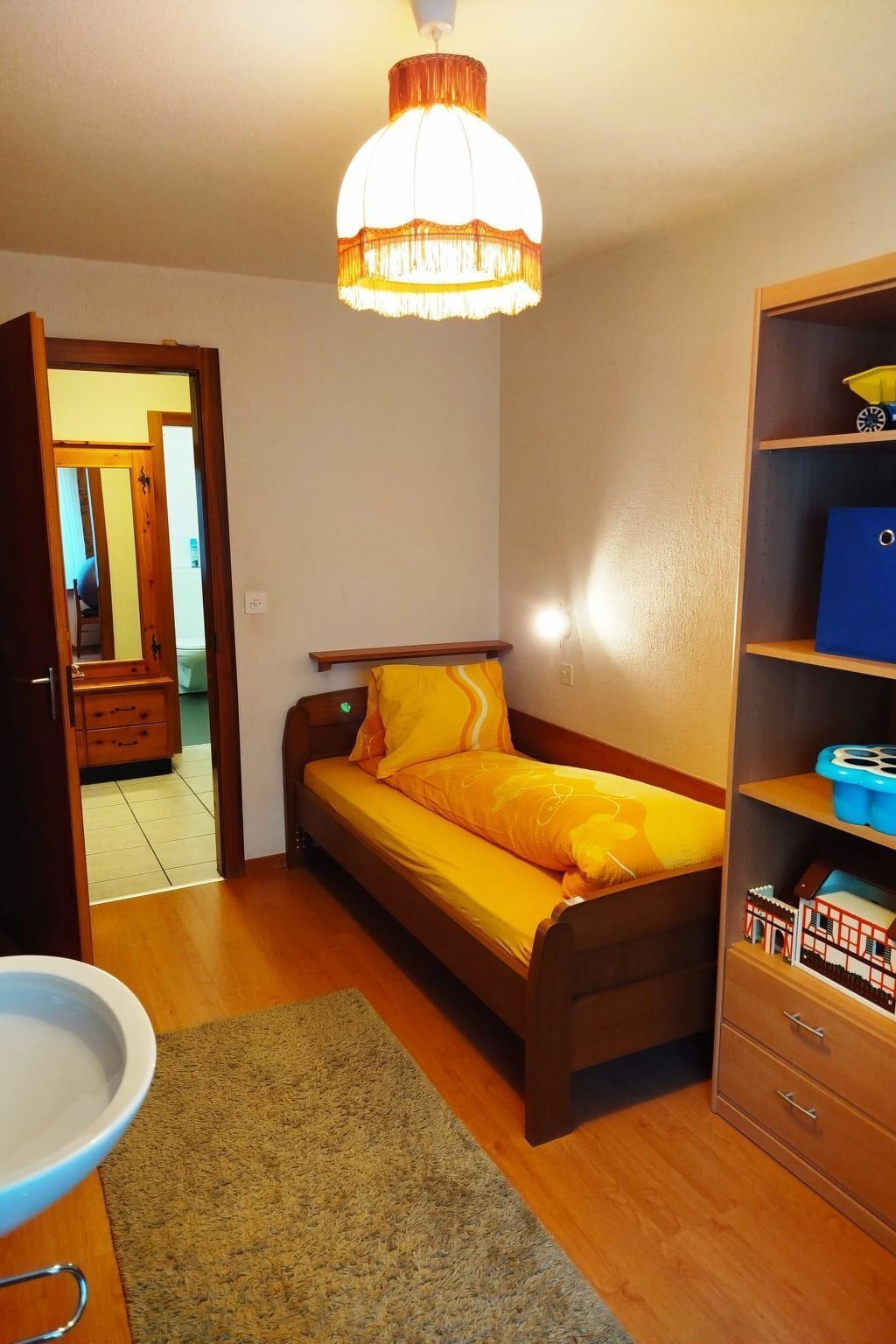 Een slaapkamer met een bed, een nachtkastje, een kledingkast, een hanglamp en een deur naar een andere kamer.