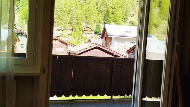 Ein Zimmer mit einer großen Schiebeglasdoor, die zu einem Hinterhof mit Holzzaun und Häusern im Hintergrund führt.