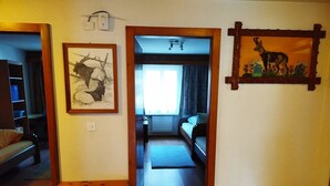 Ein Korridor, der zu einem Schlafzimmer führt, mit einem Bett, einer Holzkiste und zwei gerahmten Bildern an den Wänden.