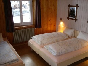 Une chambre avec deux lits, une fenêtre avec des rideaux, un radiateur et un luminaire fixé au mur.