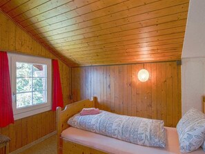 Ein Einzelbett in einer Holzhütte mit Holzwänden und einer schrägen Decke.