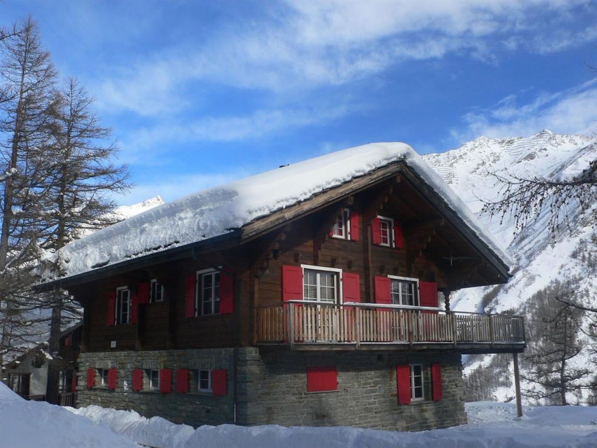 A wooden chalet with a balcony, surrounded by snow-covered mountains.