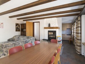 Ein Essbereich mit Holztisch und Stühlen, einer Couch, einem Kamin und einer Küche im Hintergrund.