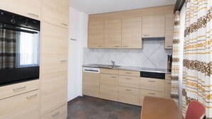 Kompakti keittiö, jossa on sisäänrakennettu uuni, astianpesukone sekä ruokailutila pöydän ja tuolien kera.