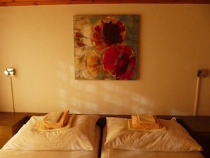 Ein Hotelzimmer mit zwei Betten, jedes mit einem Kopfkissen und einem gefalteten Handtuch.