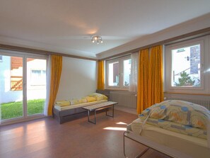 A room with a bed, a bench, and a table. There are windows with curtains. - Chalet Saasia Appartement/Fewo 9-Bettwohnung by Interhome (Saas-Fee)