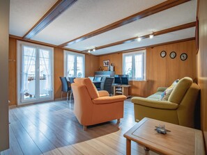 Amplia habitación con techo de madera, zona de comedor con sillas, un sofá y una pequeña mesa.