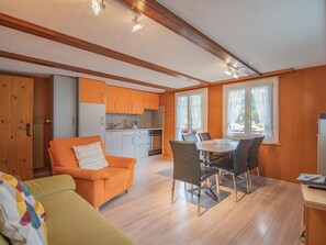 A modern kitchen with wooden cabinets, a dining area with a table and chairs, and a living room with a sofa and a chair. - Chalet Alpenruh Appartement/Fewo Nr. 2 Mittaghorn by Interhome (Saas-Fee)