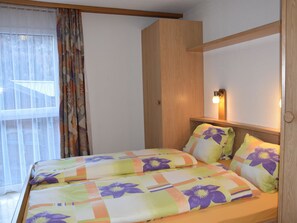 A hotel room with a bed, a window with curtains, a wall-mounted light, and a wooden headboard. - Daniela Appartement/Fewo 4-Bettwohnung by Interhome (Saas-Fee)