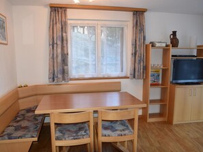 A cozy room with a wooden bench, a table, and chairs. There is a window with curtains, a television on a stand, and a bookshelf. - Daniela Appartement/Fewo 4-Bettwohnung by Interhome (Saas-Fee)
