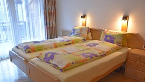 Una cama doble con una colcha estampada con flores, dos mesitas de noche y una mesita auxiliar con una lámpara.