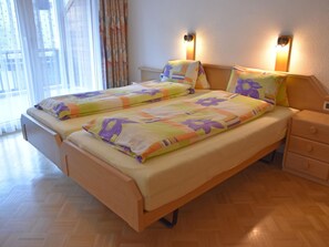 A double bed with a floral bedspread, two bedside tables, and a nightstand with a lamp. - Daniela Appartement/Fewo 4-Bettwohnung by Interhome (Saas-Fee)