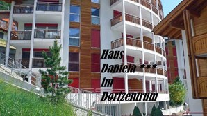 Un edificio de varios pisos con balcones, una escalera y un letrero que dice 'Haus Daniela im Dorfzentrum'.