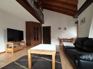 A living room with a television, wooden furniture, a black leather sofa, and a staircase. - Etzel Appartement/Fewo 12-Bettwohnung by Interhome (Saas-Fee)