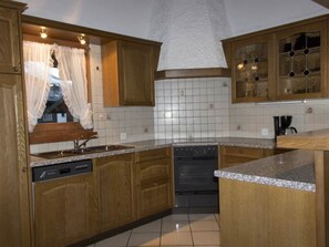 Cozinha com armários de madeira, lava-louças, forno e janela com cortinas.