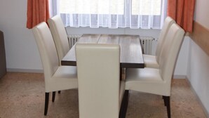 Een zithoek met een tafel en vier stoelen, een raam met gordijnen en een radiator onder het raam.