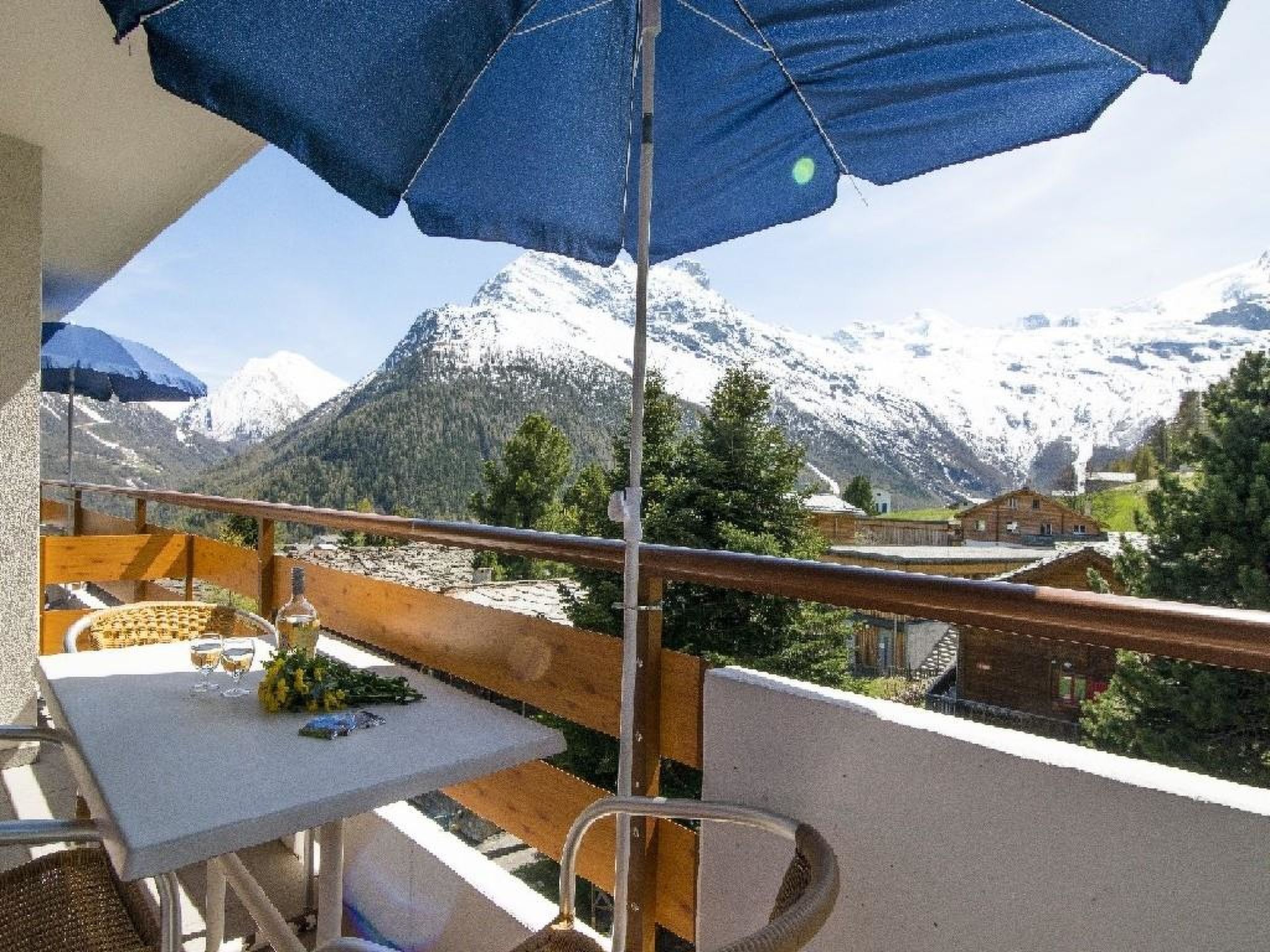 A balcony with a table and chairs, overlooking snow-capped mountains.
