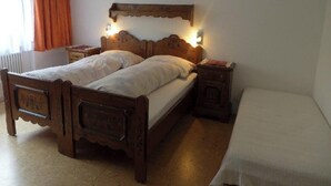 Een houten tweepersoonsbed met hoofdeinde, twee nachtkastjes en een eenpersoonsbed in de aangrenzende kamer.