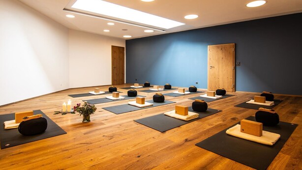Ein Yoga-Studio mit Holzboden, schwarzen Yogamatten und Holzblöcken, bereit zum Üben.