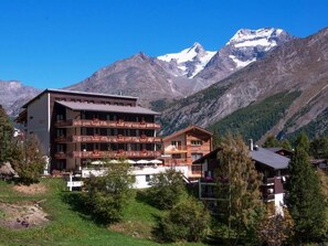 A multi-story hotel with balconies, set against a backdrop of snow-capped mountains. - Apartment Bristolino Appartement/Fewo, Dusche, WC, Terrasse by Interhome (Saas-Fee)