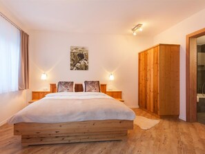 Quarto com cama de madeira, duas luminárias de cabeceira, um quadro na parede e um guarda-roupa de madeira.