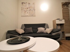 A modern living room with a grey sofa, a small round table, and a wall-mounted light. - Chalet Ideal Appartement/Fewo 3-Bettwohnung Nr. 3 by Interhome (Saas-Fee)