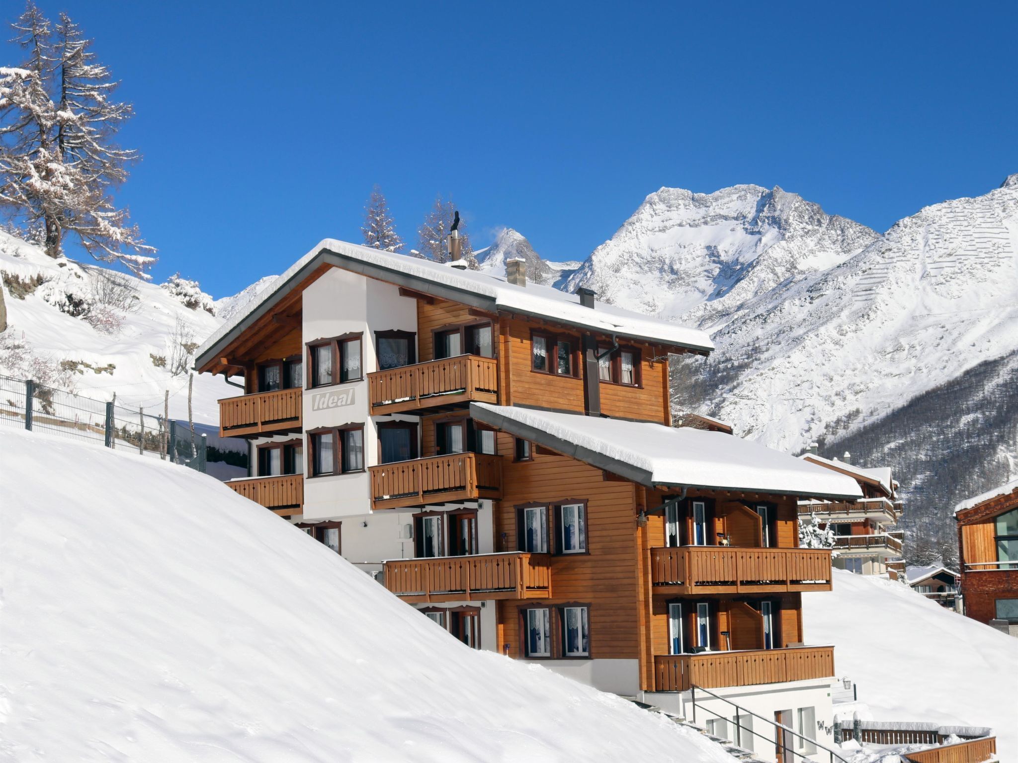 Een hotel met meerdere verdiepingen, houten balkons, een met sneeuw bedekte dak en een bergachtige achtergrond.