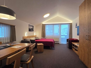 Hotellihuone, jossa on sänky, työpöytä, tuoli, puinen vaatekaappi ja ikkuna, jossa on verhot.