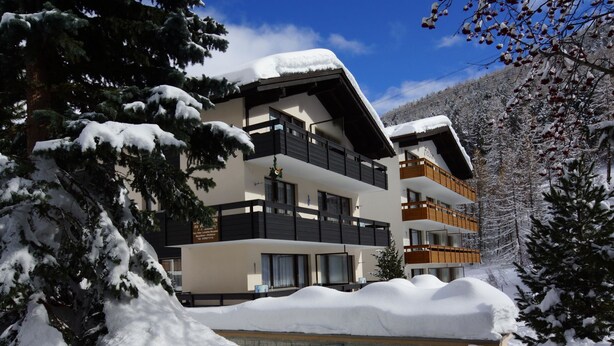 Ein mehrstöckiges Hotel mit Balkonen, umgeben von schneebedeckten Bäumen und einem klaren Himmel.